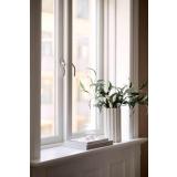 Vase, stilkblomst, bøker og telysholder i vinduskarm