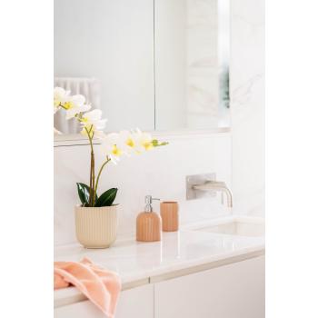 Baderom med såpedispenser, tannglass og håndkle med en orkide som pynt